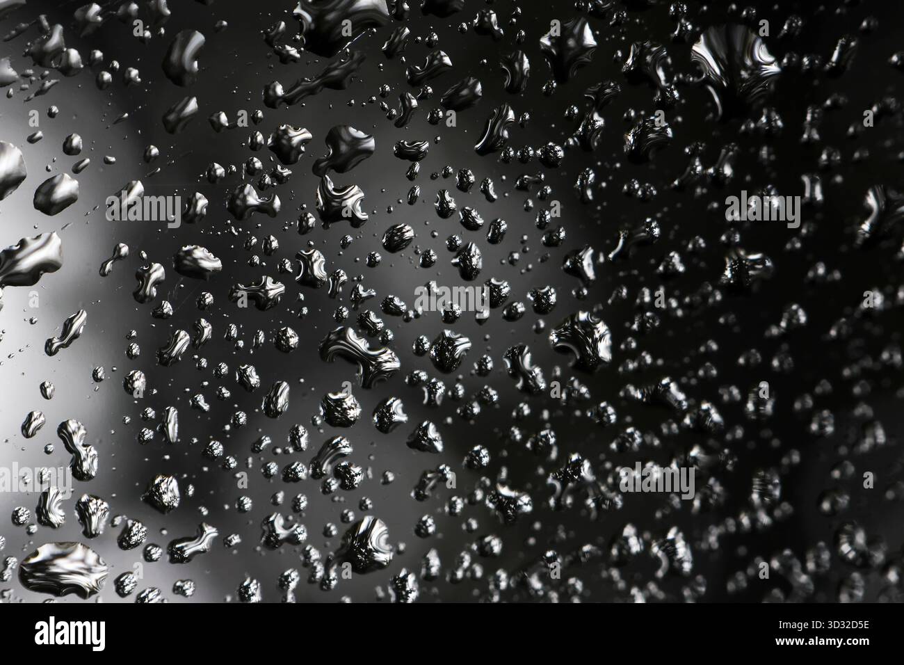 Moody abstrakter Hintergrund von Wassertropfen auf nasser schwarzer Oberfläche. Die flüssige Textur des Regens erzeugt ein ruhiges und reflektierendes Muster voller Feuchtigkeit und Kondenzen Stockfoto