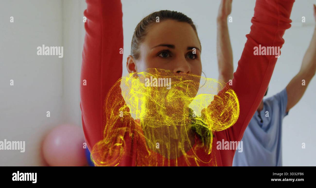 Eine Frau, die sich über dem Kopf spannt, trägt ein rotes Oberteil mit Reifen im Studio, mit rosa Kugel, gelbem Wirbel Stockfoto
