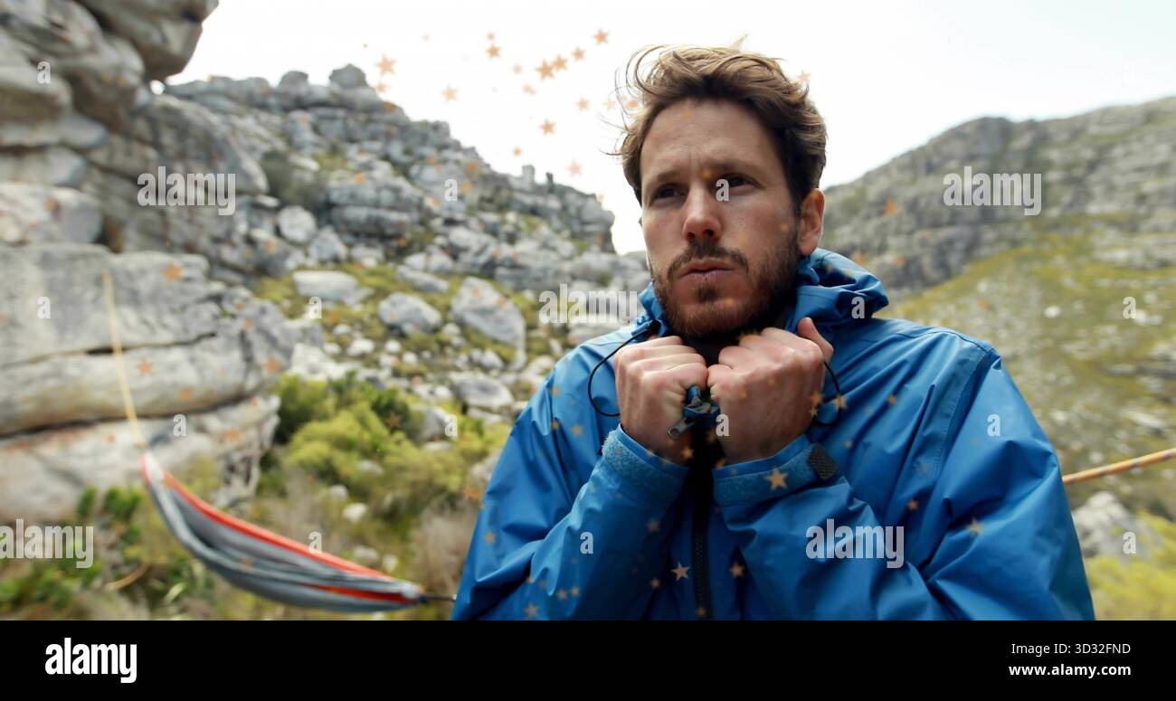 Der Mann hält einen blauen Jackenkragen auf felsigem Hang, mit gestreiftem Hängemattenseil und Felsbrocken Stockfoto