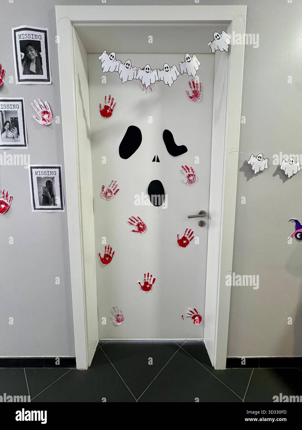 Mit Halloween-Motiven dekorierte Tür mit Gespenstergesicht, roten Handabdrücken und ausgeschnittenen Girlanden aus Papier. - Smartphone-aufgenommenes Stockfoto