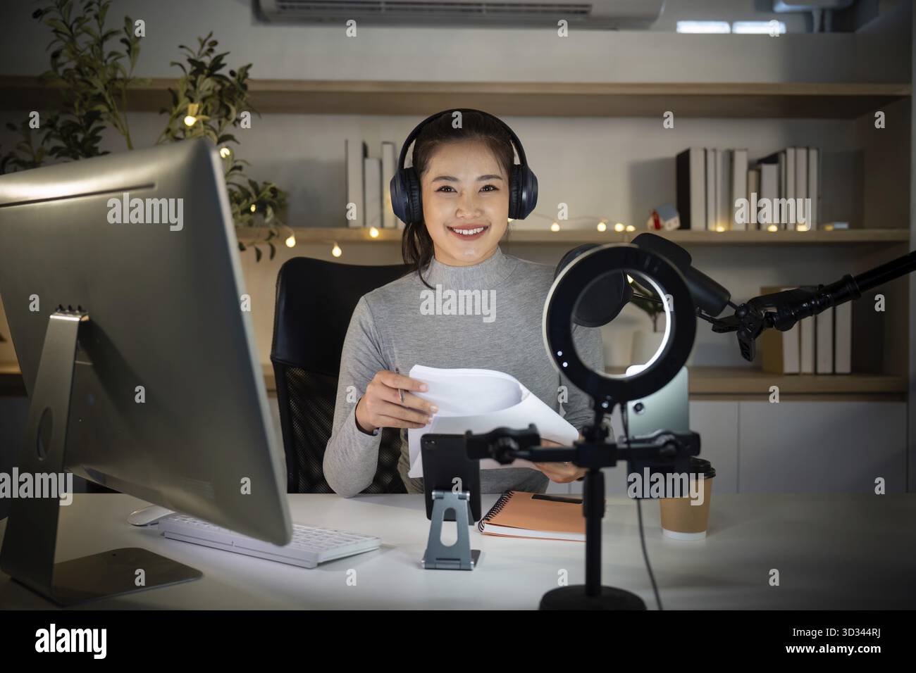 Eine junge Frau bereitet sich auf ihren Podcast vor, indem sie Notizen liest und Positivität und Begeisterung für ihre bevorstehende Aufnahme ausstrahlt Stockfoto
