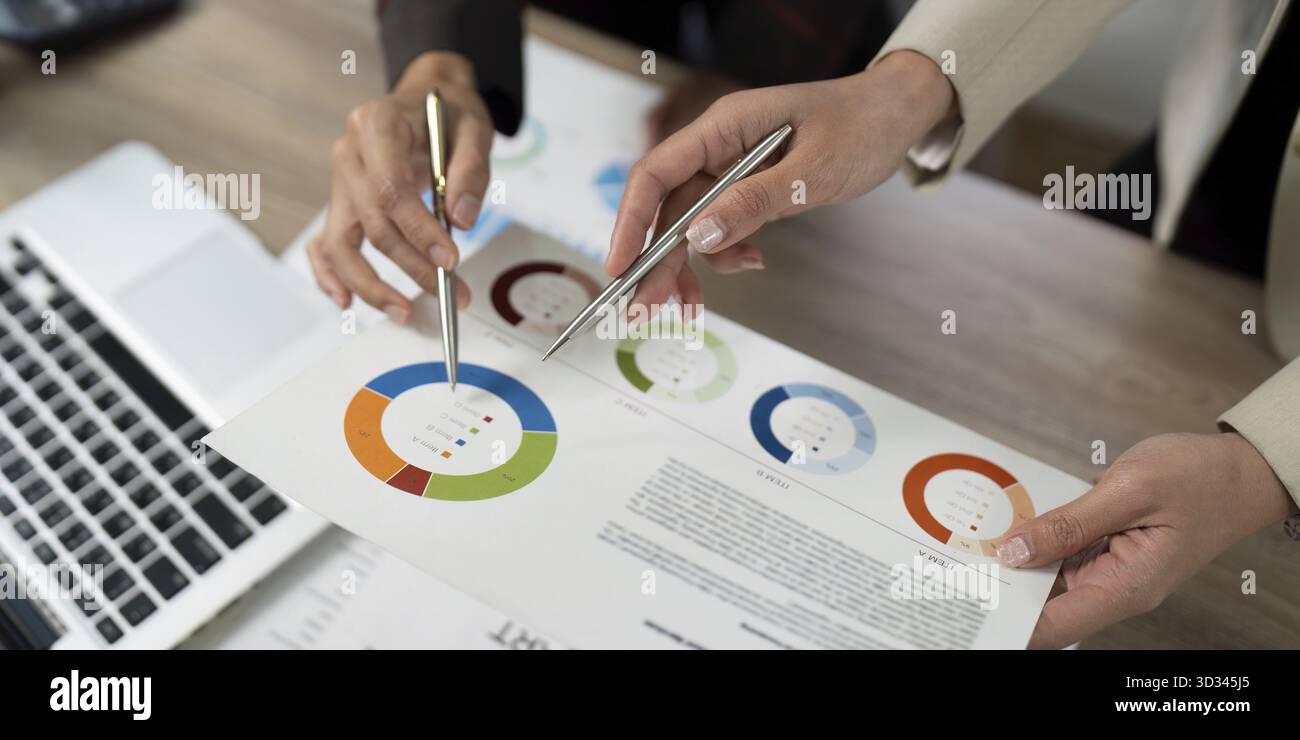 Geschäftsfrauen arbeiten an finanziellen Erkenntnissen zusammen und zeigen auf visuelle Datenberichte in einem modernen Bürobereich Stockfoto