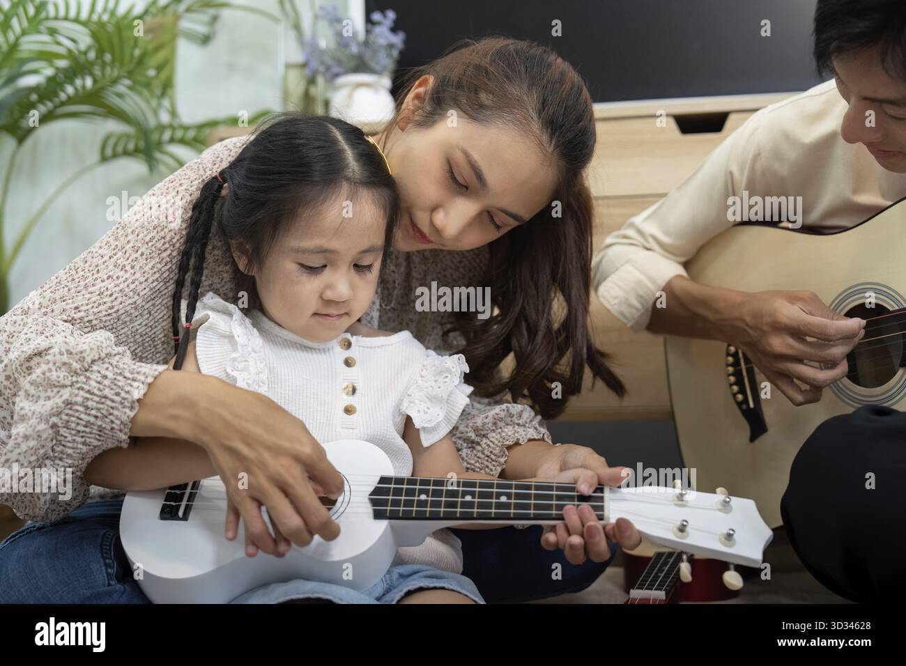 Ein pflegender Moment, in dem eine Mutter ihre Tochter beim Ukulele-Spiel begleitet und Kreativität und Liebe durch die Zeit der Familienmusik fördert Stockfoto