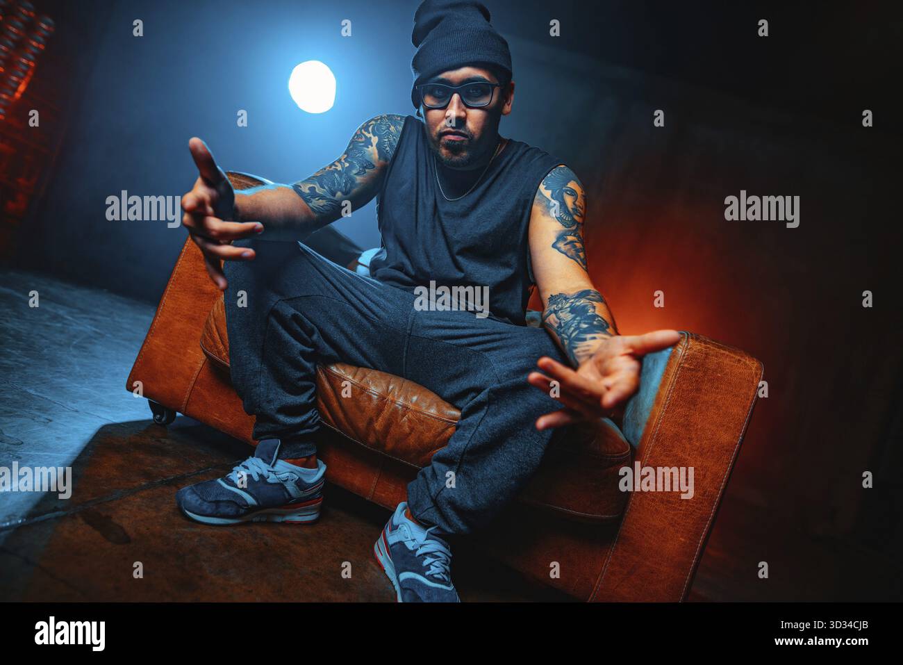 Junger Mann Breakdancer, der in einem großen alten Stuhlporträt sitzt. Tätowierung an den Händen Stockfoto