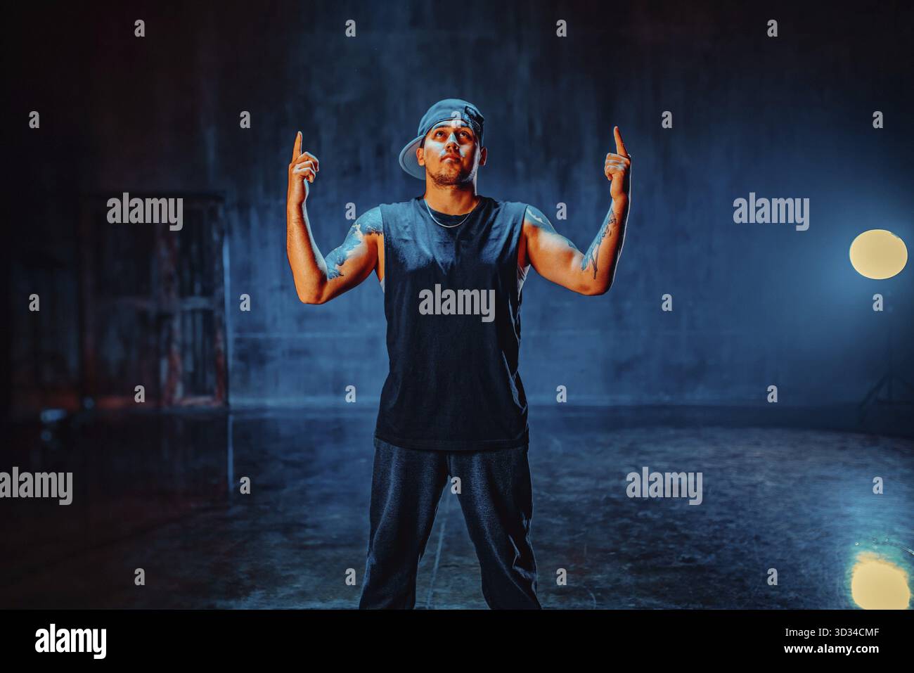 Junger Mann Breakdance Tänzer, der in dunkler Halle auf Wandhintergrund steht. Tätowierung an den Händen Stockfoto