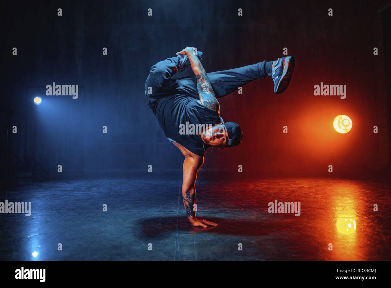 Junger Mann tanzt in dunkler Halle mit blauen und roten Lichtern. Tätowierung an den Händen Stockfoto