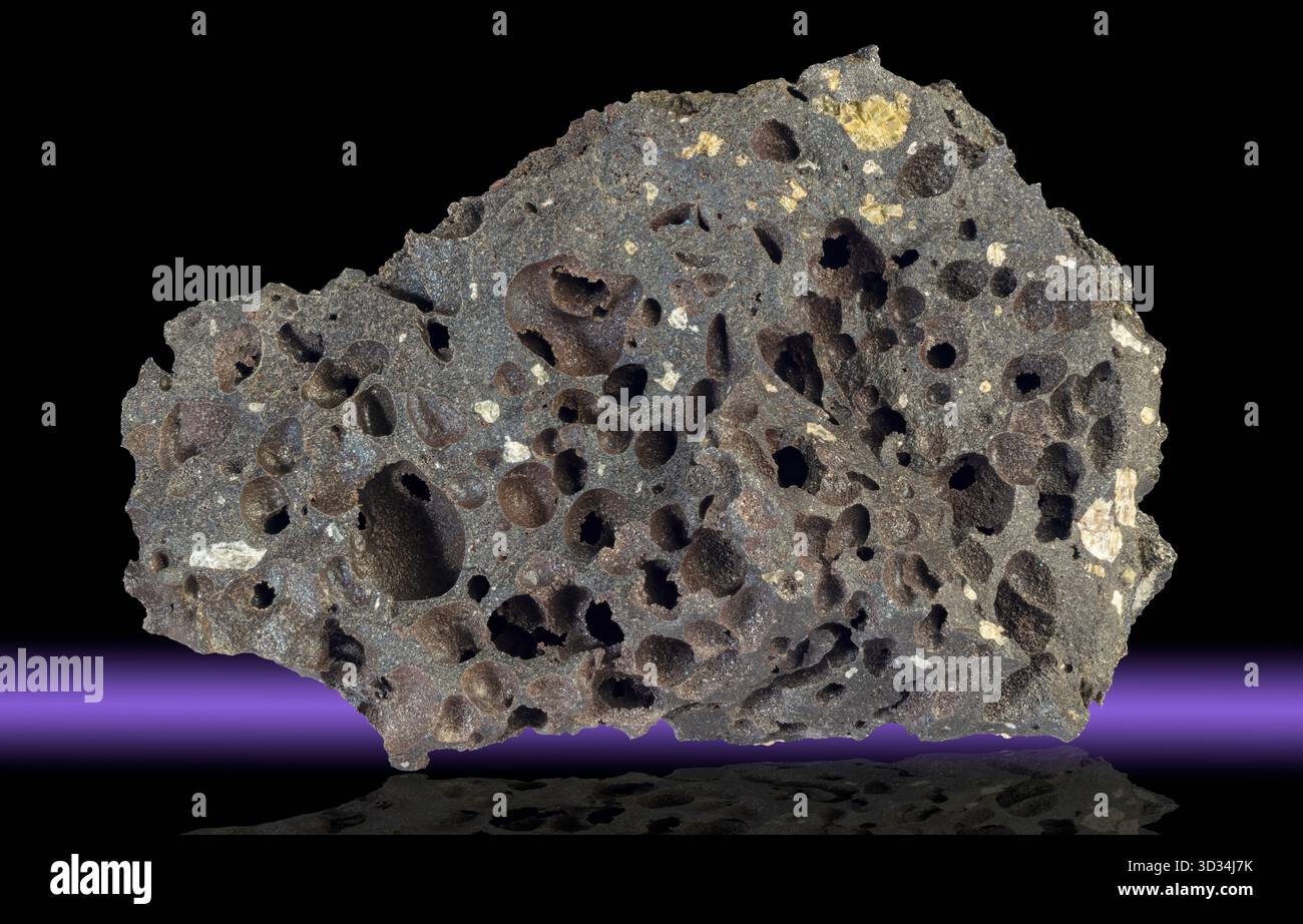 Dunkles vesikuläres Basalt aus Island, gekennzeichnet durch reichlich abgerundete Vesikeln, die durch das Entweichen vulkanischer Gase während der Eruption entstehen. Stockfoto