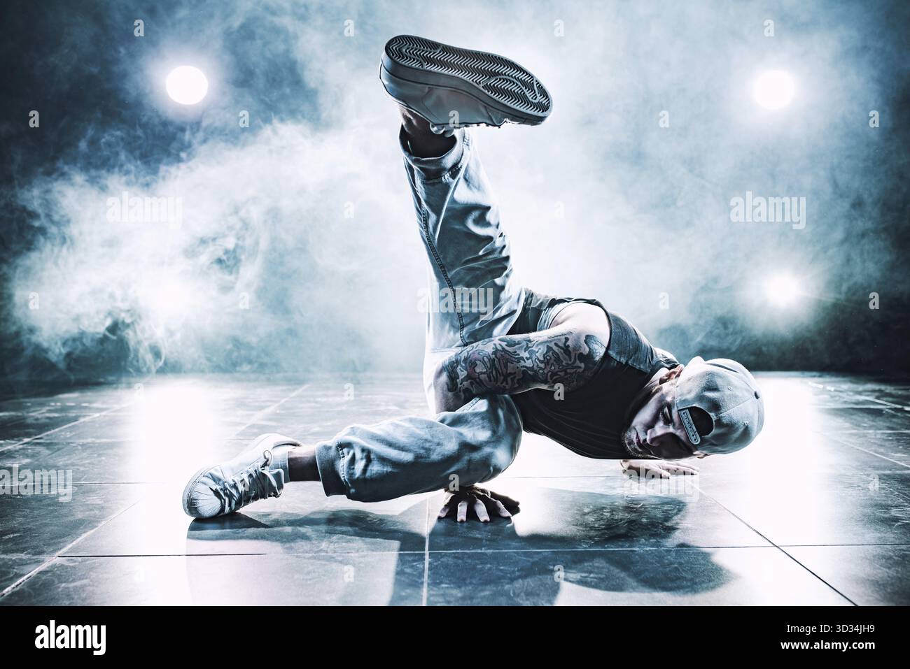 Junger Mann tanzt im Club mit Licht und Rauch. Tätowierung am Körper. Blaue Farbtöne Stockfoto