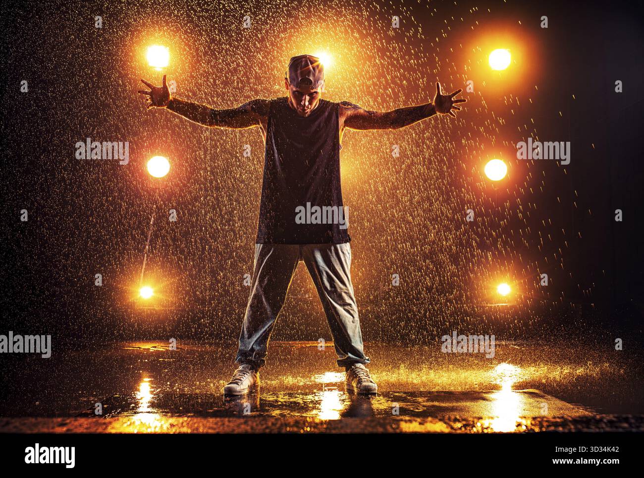 Junger Mann Breakdancer, der im Club mit Licht und Wasser steht. Tätowierung am Körper Stockfoto