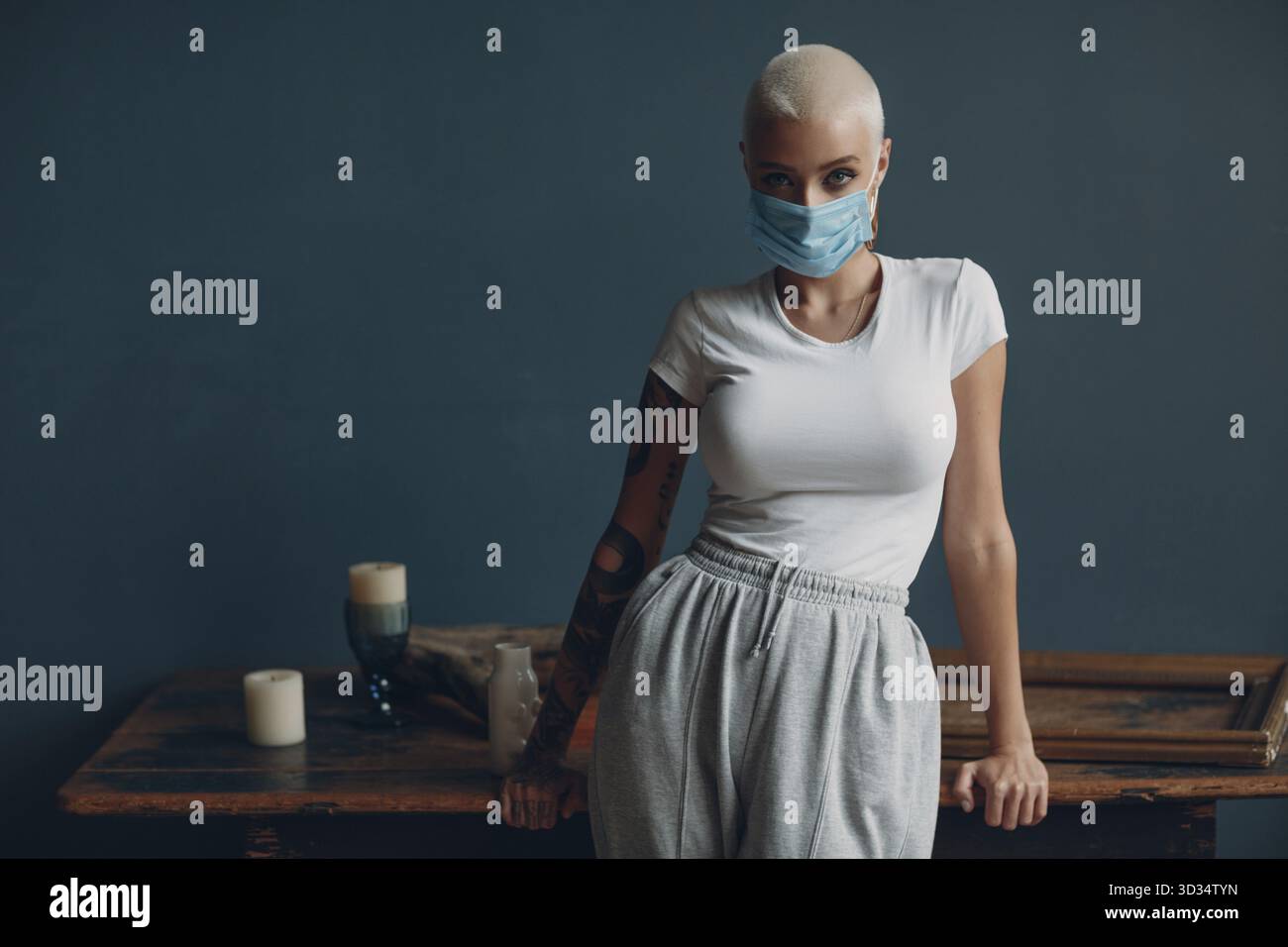 Millenial junge Frau in medizinischen Schutz Gesichtsmask mit kurzen blonden Haaren Porträt stehend Innenwohnung Stockfoto