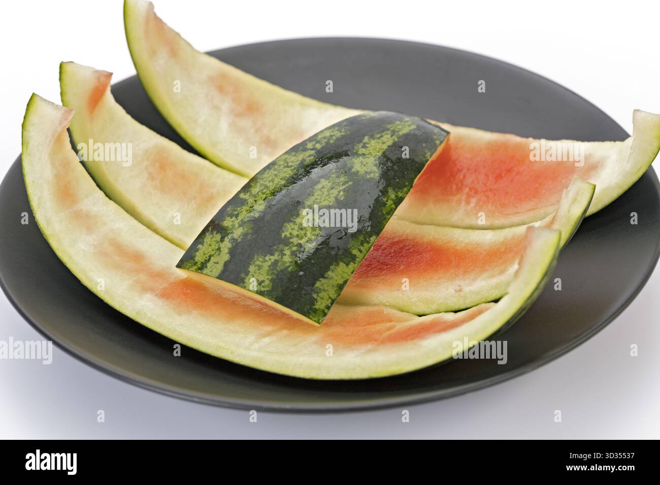 Wassermelonenschale, die auf einer schwarzen Platte mit weißem Hintergrund übrig bleibt, ist eine Zutat in der thailändischen Küche, wie z. B. kaeng Som. Stockfoto