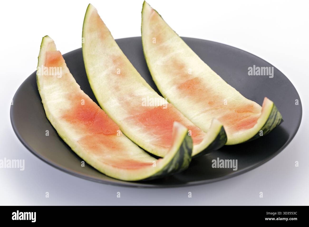 Wassermelonenschale, die auf einer schwarzen Platte mit weißem Hintergrund übrig bleibt, ist eine Zutat in der thailändischen Küche, wie z. B. kaeng Som. Stockfoto