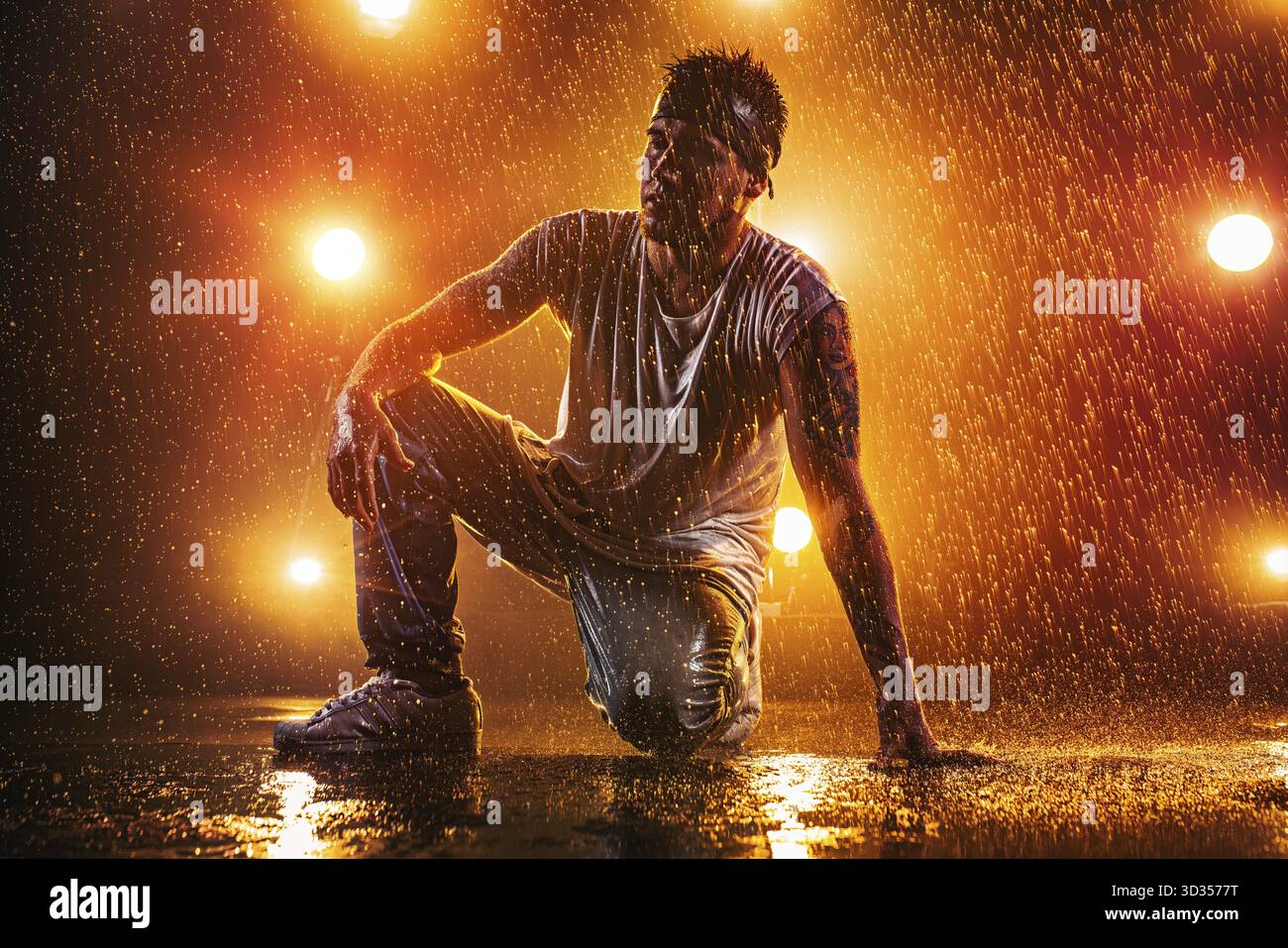 Junger Mann tanzt im Club mit Licht, Wasser und Rauch. Tätowierung am Körper Stockfoto