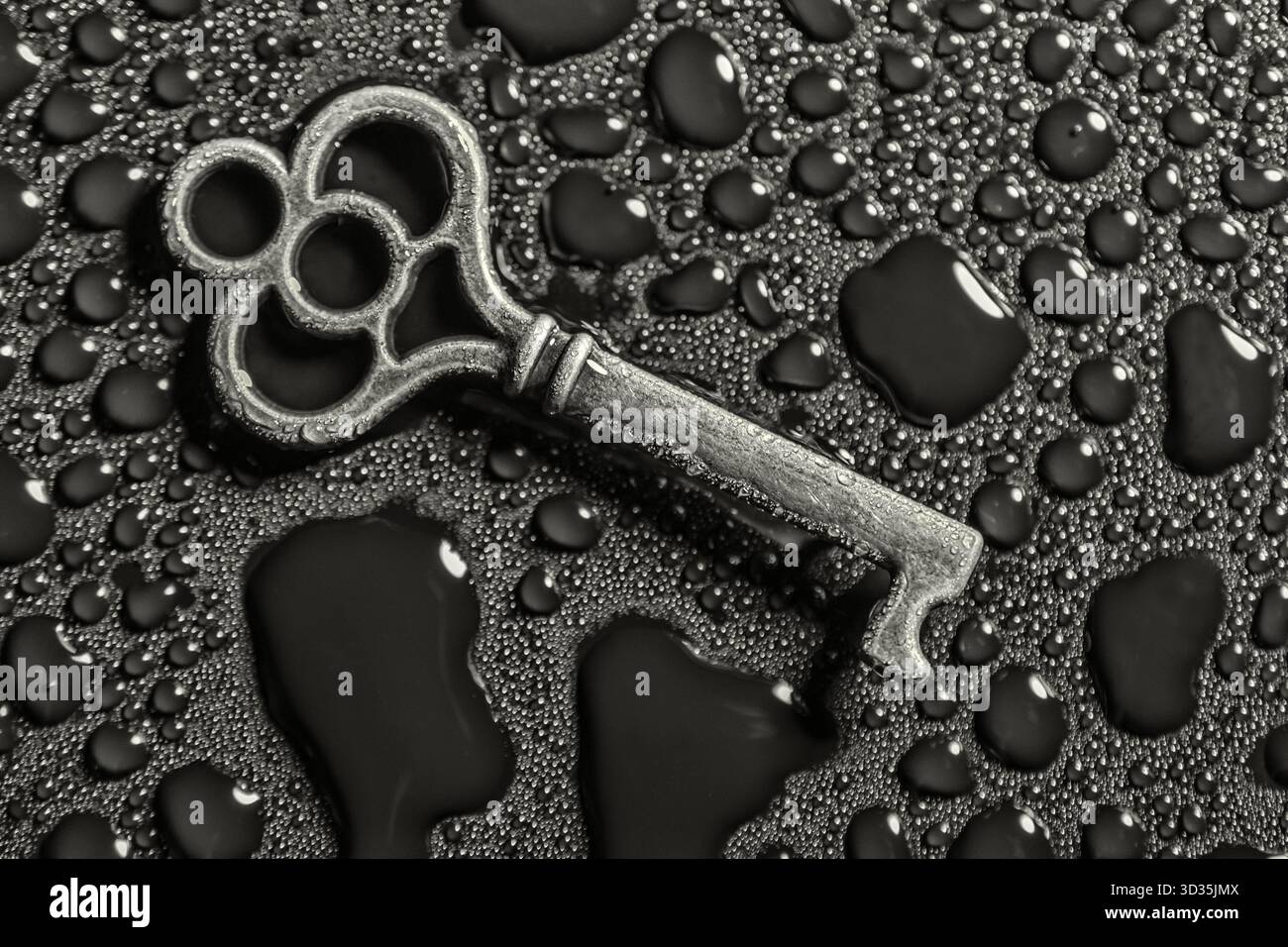 Vintage-Metallschlüssel mit kunstvollen Schlaufen auf einer mit Wassertropfen bedeckten Oberfläche. Eine symbolische und strukturierte Komposition, die Mysterium, Erinnerung und t Stockfoto