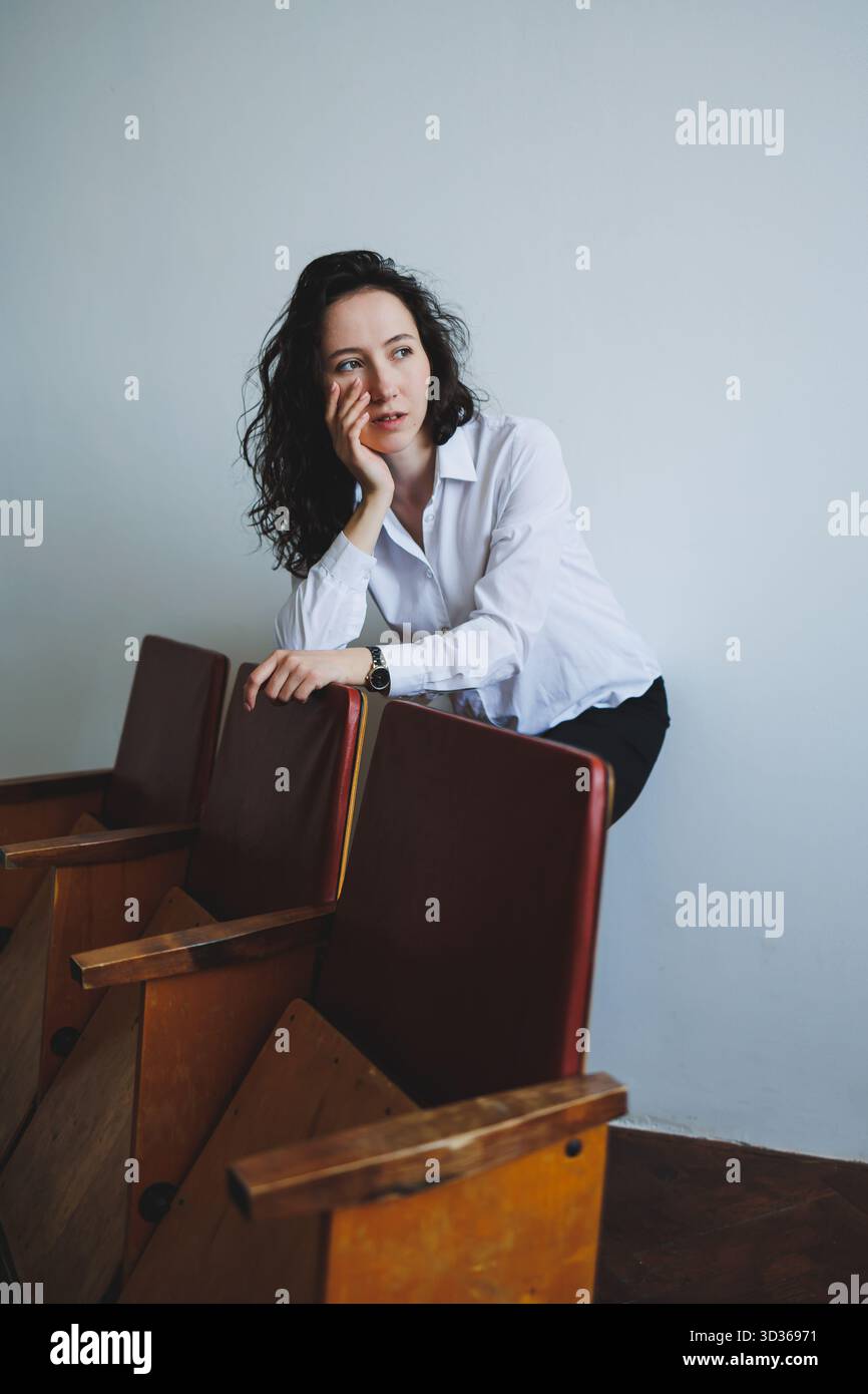 Eine nachdenkliche junge Frau, elegant in einem weißen Hemd gekleidet, posiert anmutig auf einer Vintage-Bank und kreiert innerhalb eines C eine inspirierende und künstlerische Szene Stockfoto