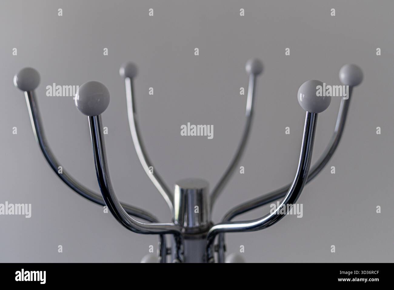 Ein eleganter Kleiderständer aus Chrom steht vor einer grauen Wand und besticht durch ein minimalistisches Design. Stockfoto