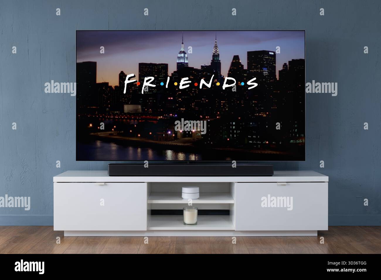 Ein Breitbild-OLED-Fernseher, der die Intro-Szene den Freunden der TV-Serie aus den 90er Jahren zeigt, die in einem modernen Wohnzimmer zu sehen ist. Stockfoto