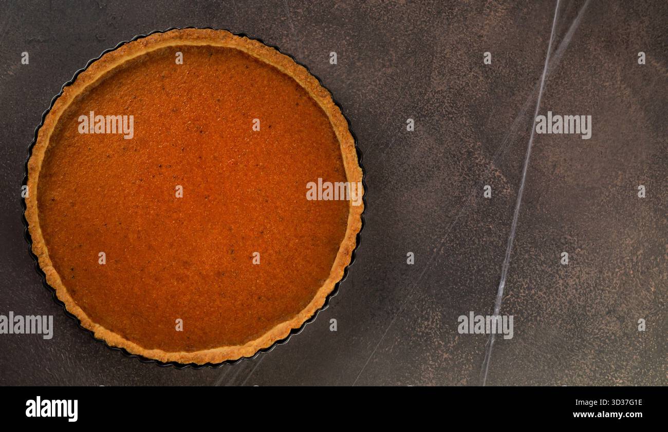 Ein frisch gebackener Kürbiskuchen sitzt auf einer dunklen Arbeitsplatte und kühlt ab. Die üppige Füllung glitzert und lädt zu festlichen Feiern und herzlichen Zusammenkünften ein Stockfoto