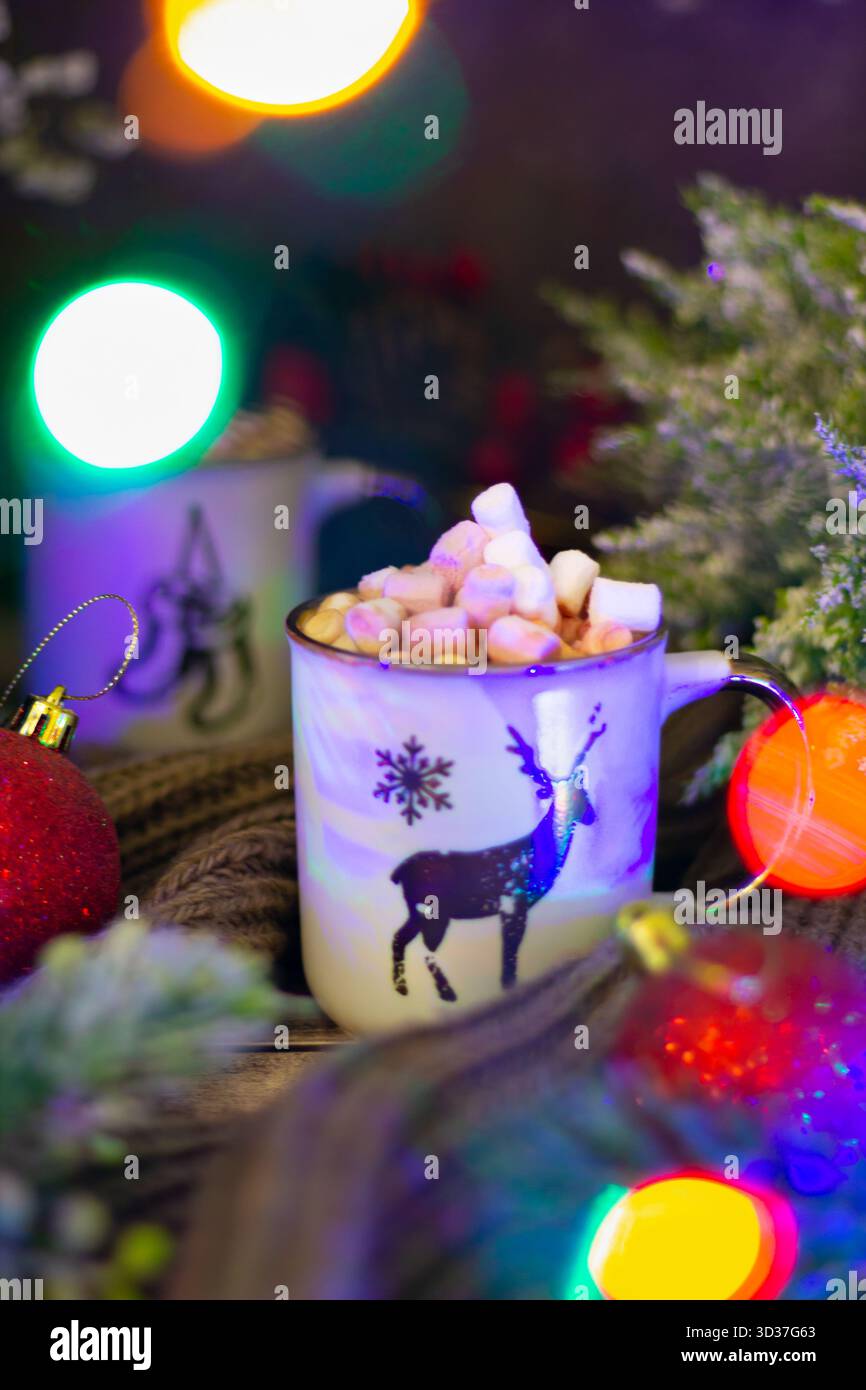 Ein warmer Becher heißer Schokolade mit flauschigen Marshmallows liegt zwischen festlichen Ornamenten und Grün und schafft eine gemütliche Winteratmosphäre, die perfekt für die holi ist Stockfoto