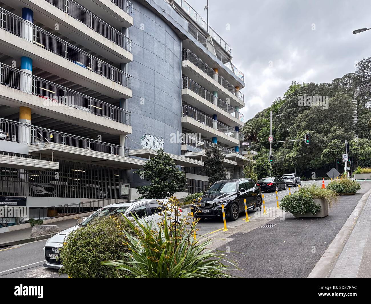 Mehrstöckiges Parkhaus in Auckland, Neuseeland, mit Autos auf einer Stadtstraße und einem üppig grünen Hügel unter bedecktem Himmel, das Urban in repräsentiert Stockfoto