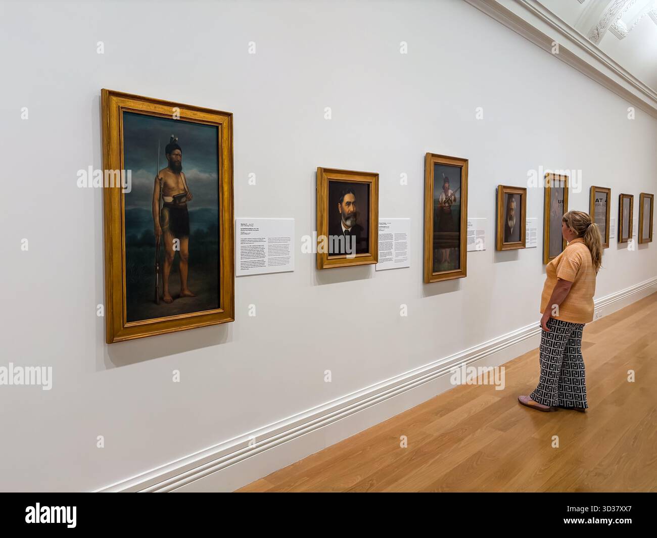 Besucher der Auckland Art Gallery sehen eine Reihe von gerahmten Porträts, darunter ein bemerkenswertes Gemälde eines Māori-Mannes, das auf einer weißen Wand im Raum ausgestellt ist Stockfoto