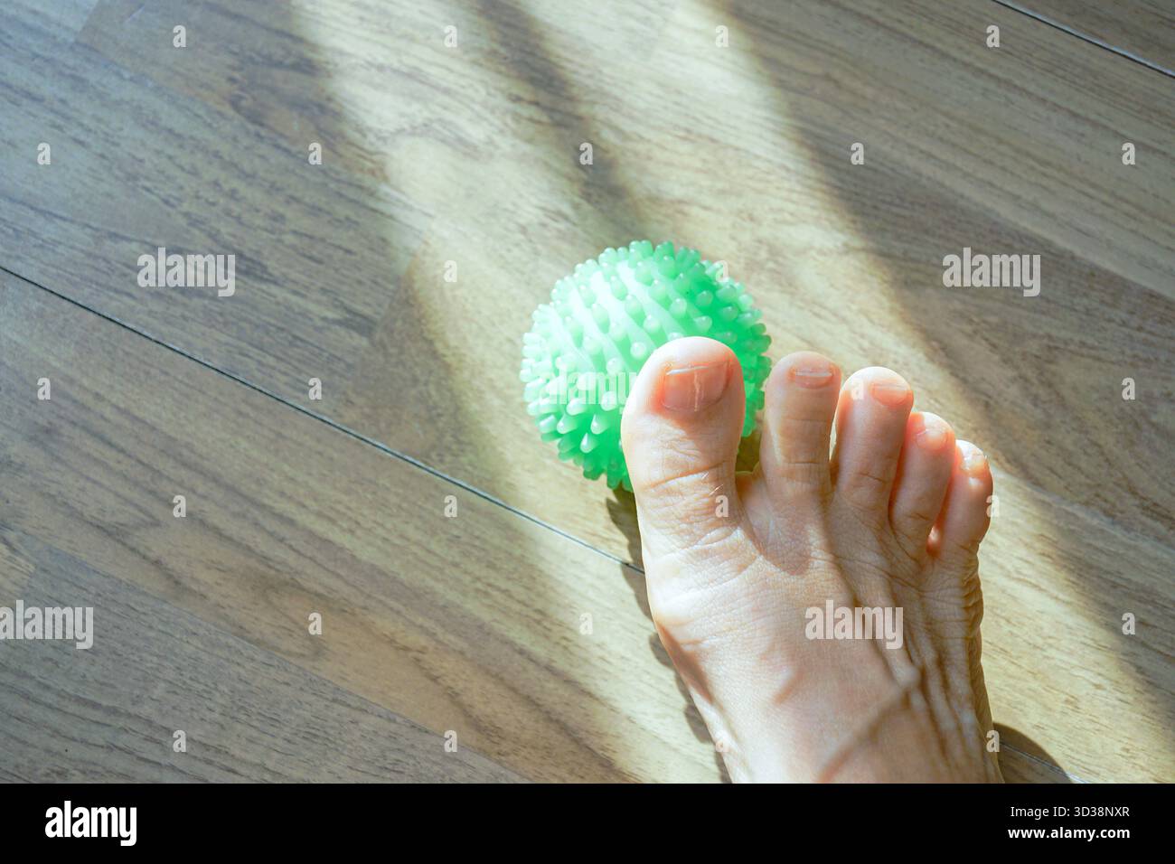 Der Fuß befindet sich neben einem strukturierten Massageball auf dem Boden im Sonnenlicht. Konzepte der Reiserückgewinnung, -Entspannung und -Entlastung nach lä Stockfoto