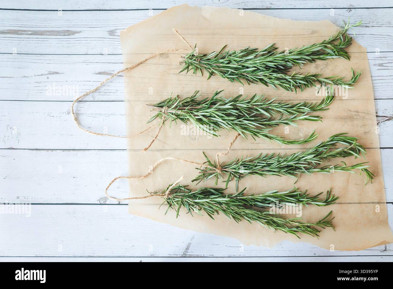 Vier Rosmarinbündel, zum Trocknen vorbereitet, gestylt auf Pergamentpapier mit hölzernem Hintergrund. Perfekt für saisonale Rezepte oder Kräuterhandwerk Stockfoto