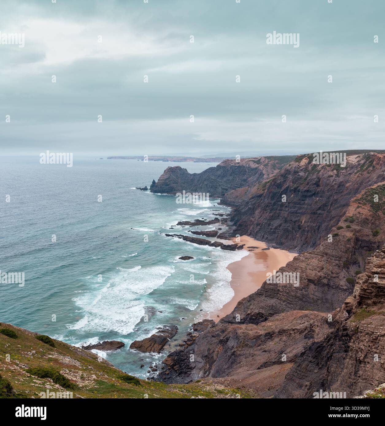 Sandstrand mit felsigen Bergrücken trübes Wetter Aussicht auf Sommer Atlantic an der felsigen Küste (Costa Vicentina, Algarve, Portugal). Und Ocean Surf Wellen. Stockfoto