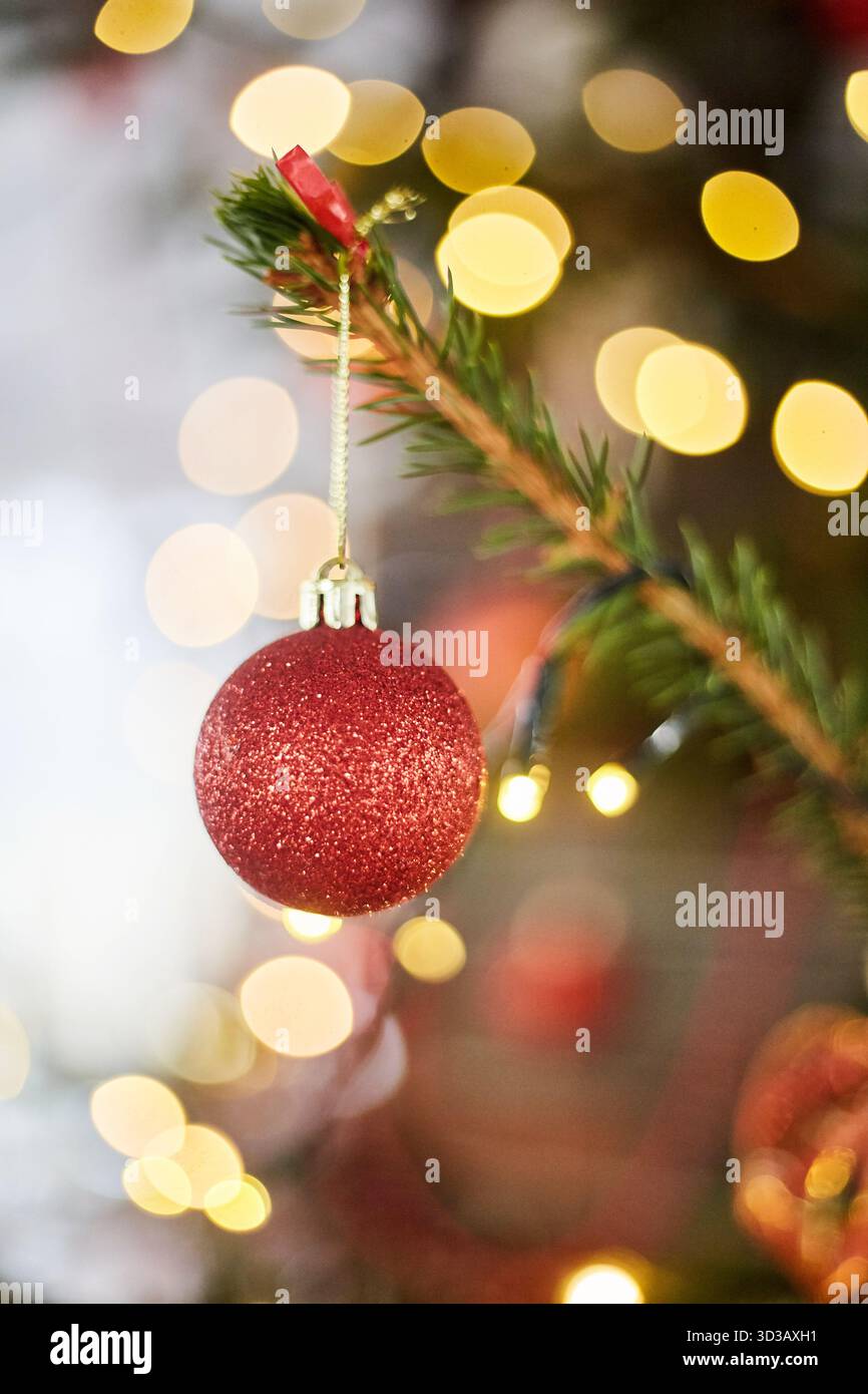 Der rote Ball auf einem Weihnachtsbaum. Weihnachtsglasspielzeug auf Bokeh-Hintergrund mit Girlanden Stockfoto