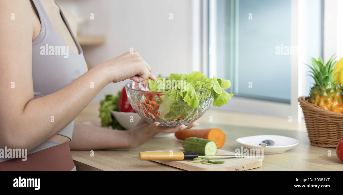 Eine Frau bereitet einen lebendigen Salat zu, der Wellness und gesunde Essgewohnheiten in ihrer Küche fördert Stockfoto