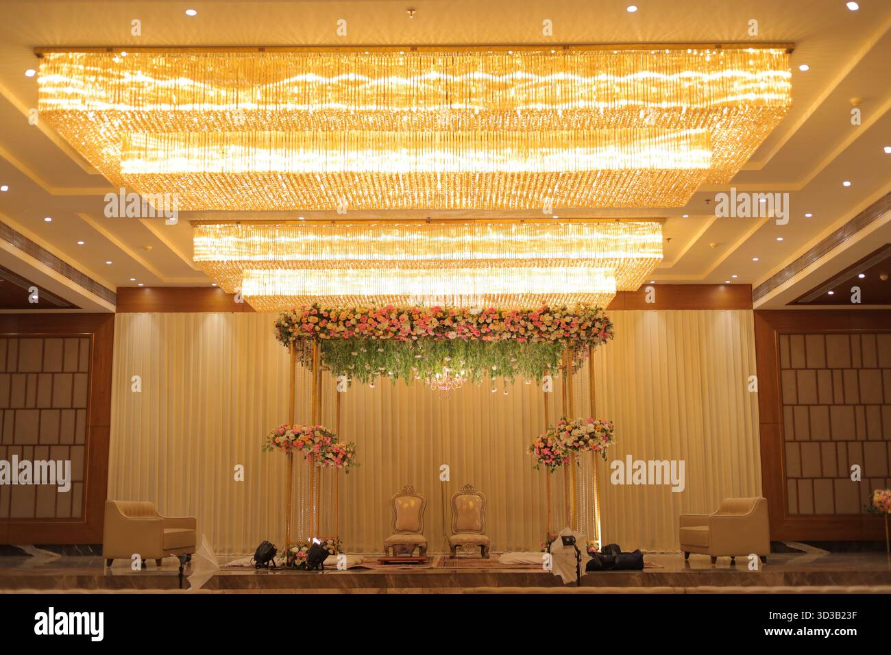 Luxuriöse indische Hochzeitsbühne mit eleganten Kronleuchtern, Blumenarrangements und goldener Beleuchtung Stockfoto