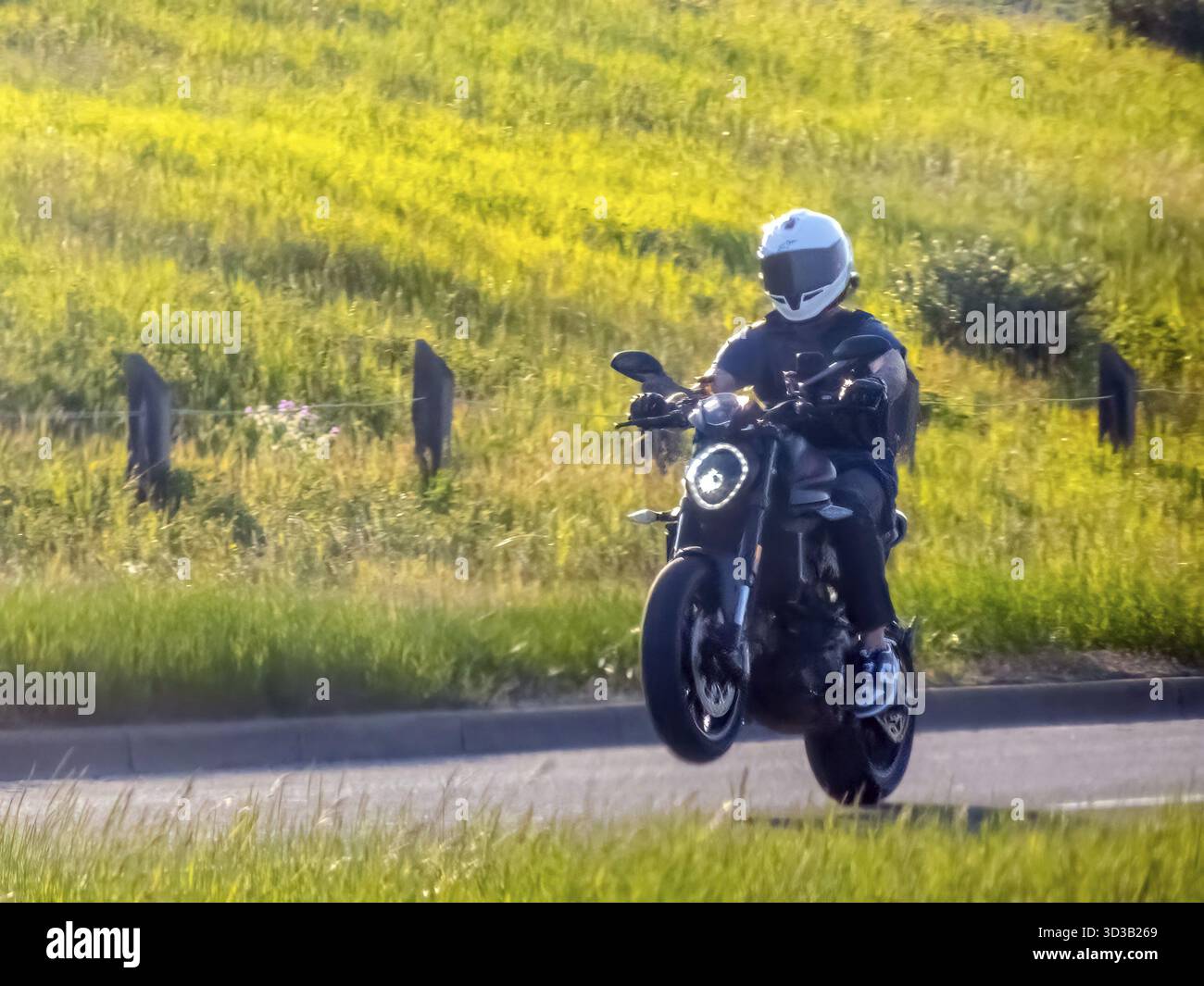 Calgary, Alberta, Kanada. Juni 2025. Ein Motorradfahrer auf einem schlanken dunklen Motorrad führt einen Wheelie auf einer Asphaltstraße durch und bietet aufregende Leistung und Stockfoto