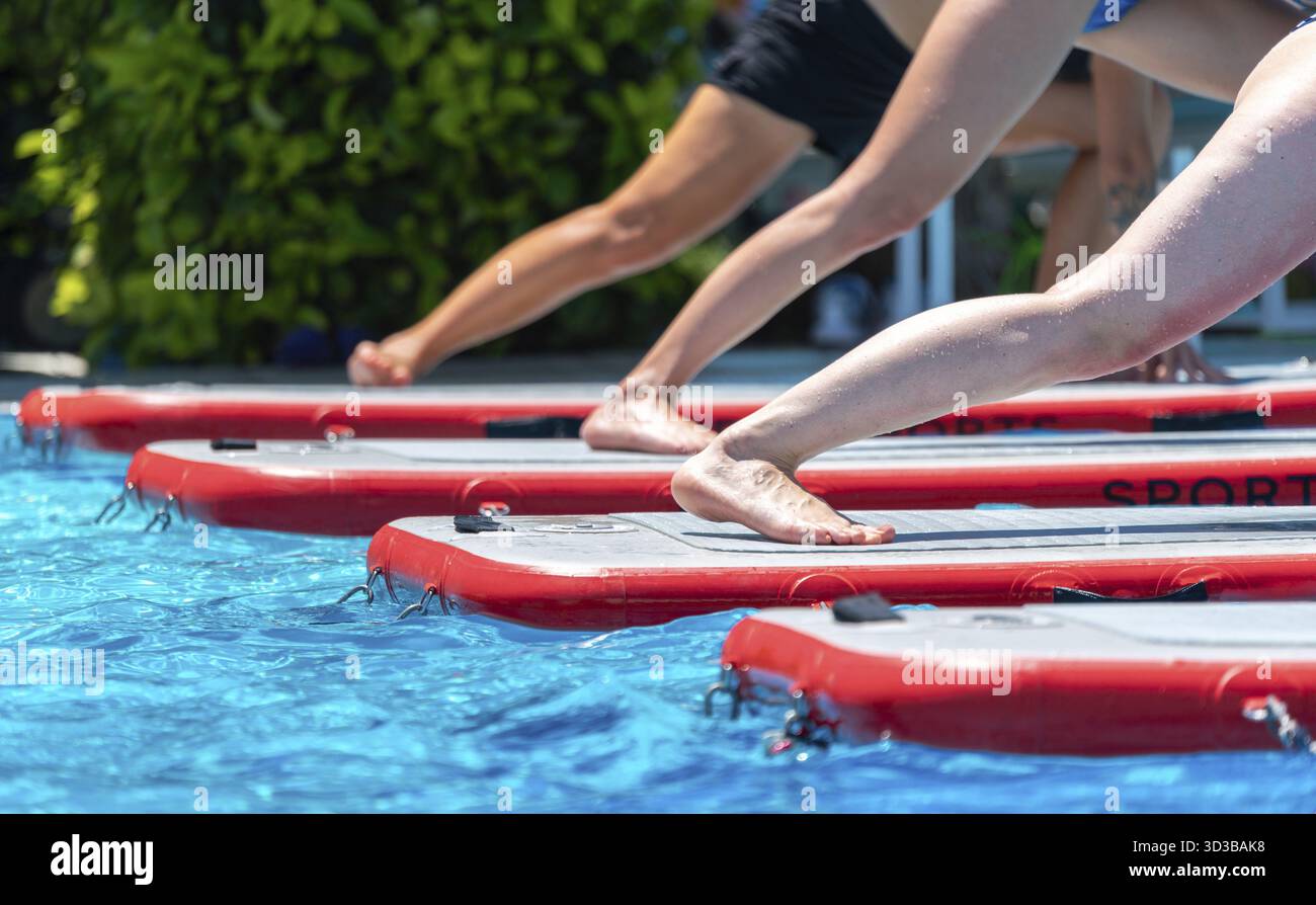 Die Füße balancieren auf Paddleboards in einem klaren Pool unter der Sonne und bieten Fitness und Balance-Training im Freien. Wellness- und Freizeitkonzept Stockfoto