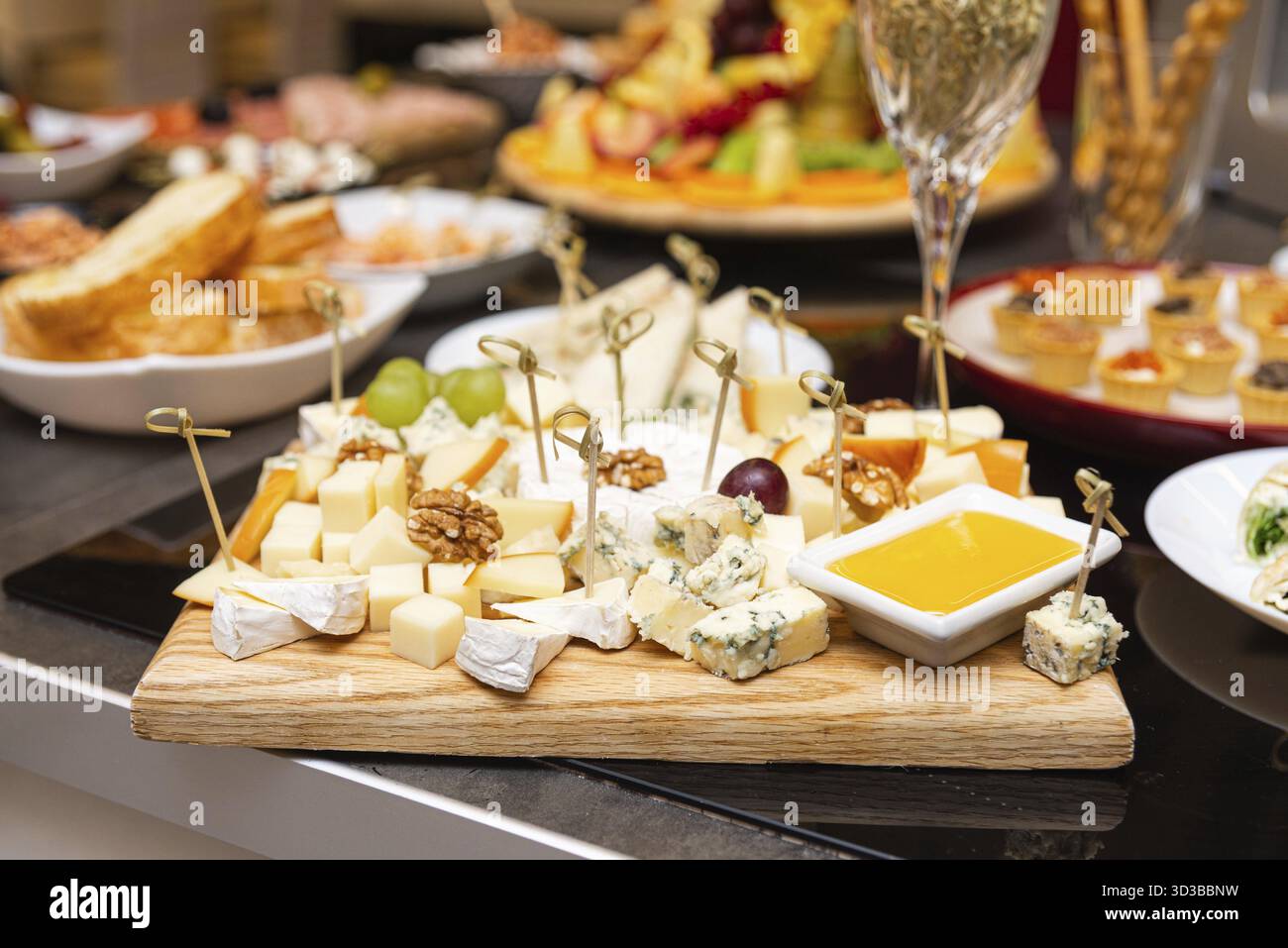 Essen, elegante Käseplatte mit verschiedenen Käsesorten, Walnüssen, Trauben und Honigdip, perfekt für Partys oder Weinverpflegung Stockfoto