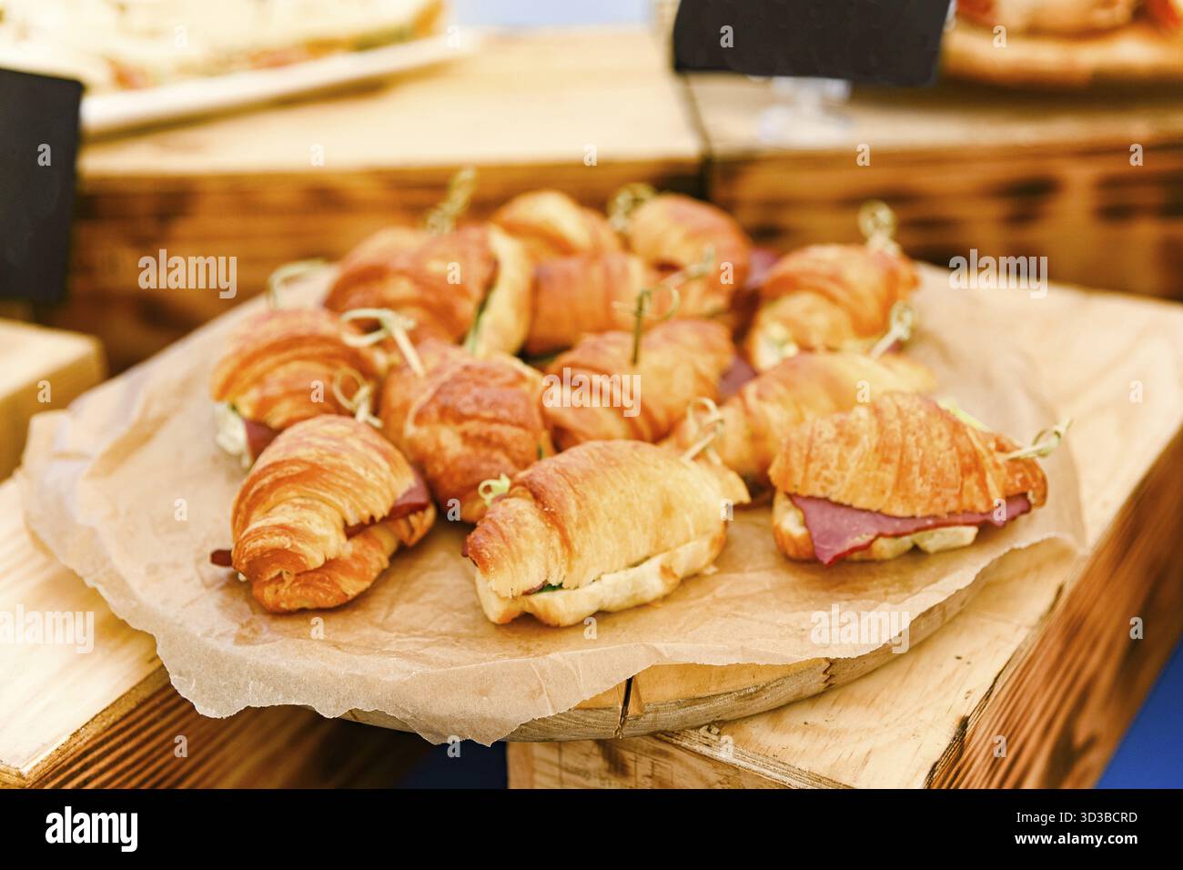 Essen, Nahaufnahme von frisch zubereiteten Mini-Croissant-Sandwiches gefüllt mit Feinkostfleisch und Gemüse, auf Pergament für Catering-Service Stockfoto