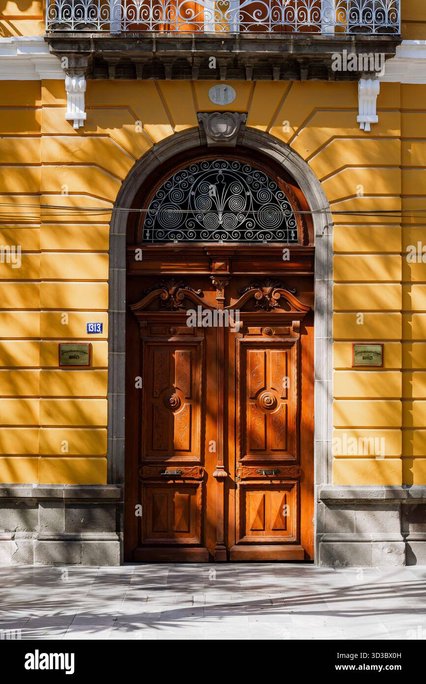 Vertikale vordere Aufnahme einer aufwendigen Holztür in einem Bogen, auf einer hellgelben Kolonialfassade mit schmiedeeisernen Details. Stockfoto