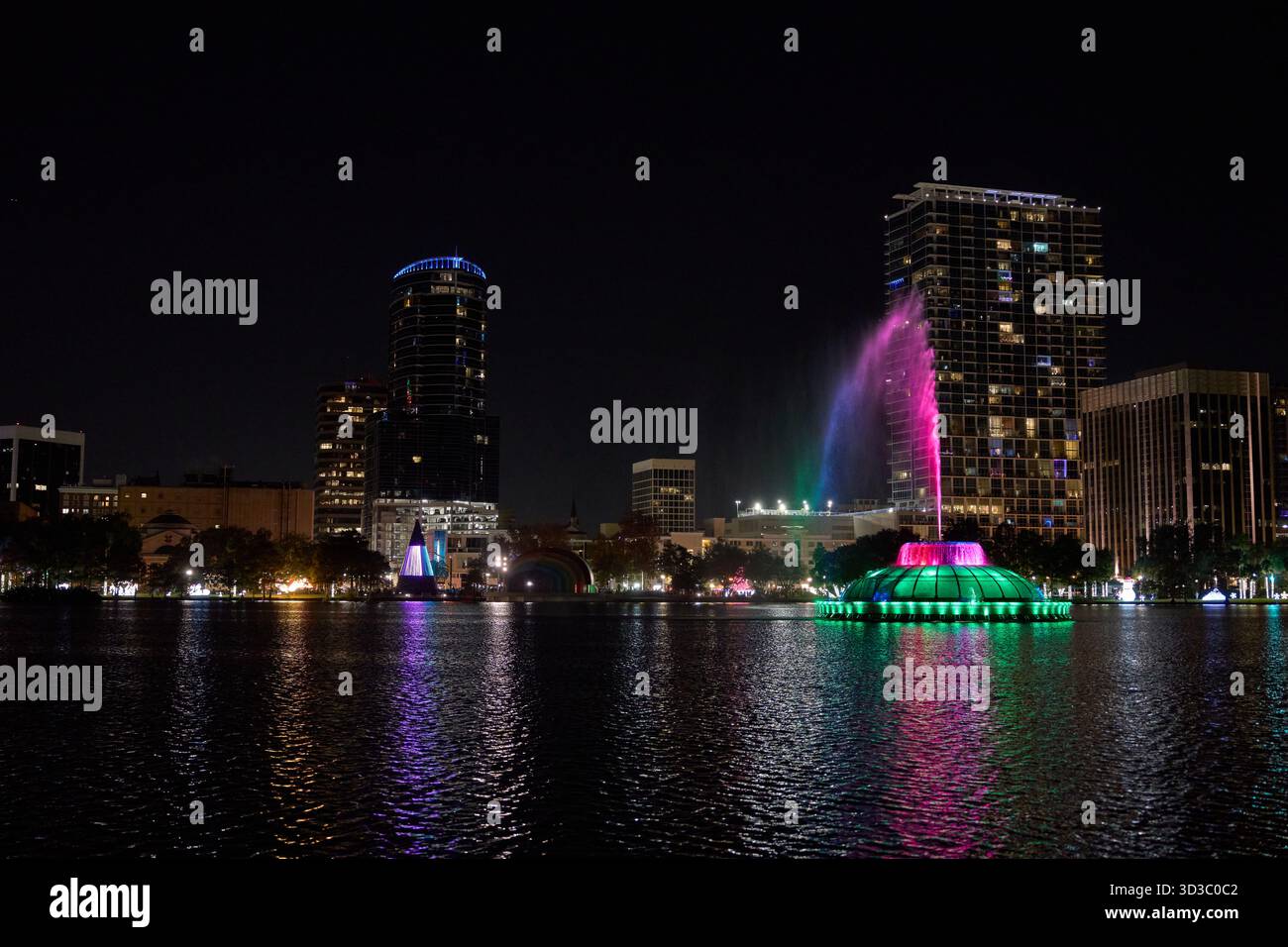Ein weites Stadtpanorama zeigt einen leuchtenden Brunnen und bunte Lichter über dem Wasser. Türme und Hochhäuser erstrahlen in einer ruhigen Nachtszene. Stockfoto