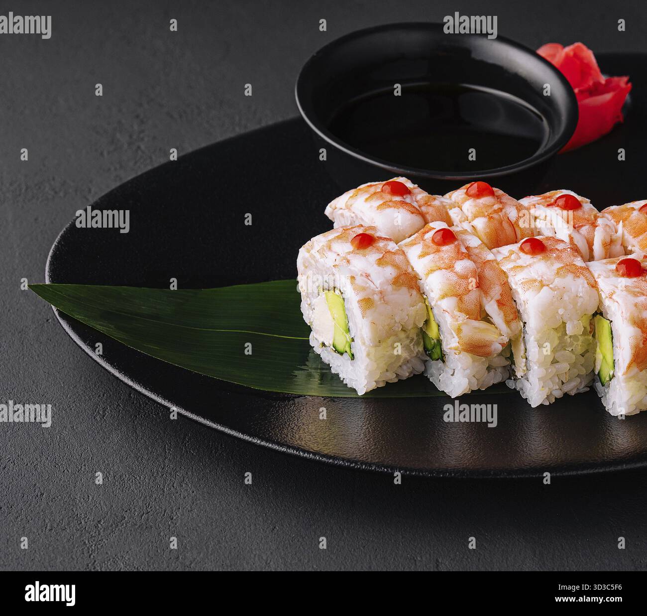 Essen, Sushi-Rolle bedeckt mit Garnelenfleisch auf schwarzer Keramikplatte Stockfoto