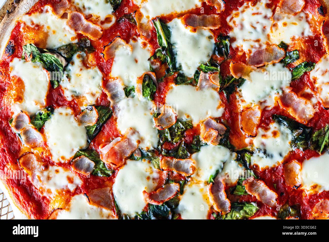 Pizza mit Speck, Tomaten, Spinat und Käse, Nahaufnahme. Strukturierter Pizza-Hintergrund. Hochwertige Fotos Stockfoto