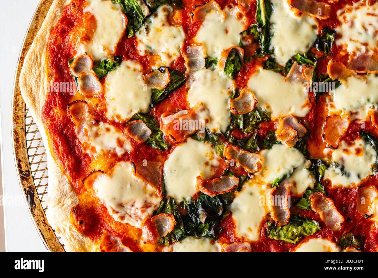 Pizza mit Speck, Tomaten, Spinat und Käse, Nahaufnahme. Strukturierter Pizza-Hintergrund. Hochwertige Fotos Stockfoto