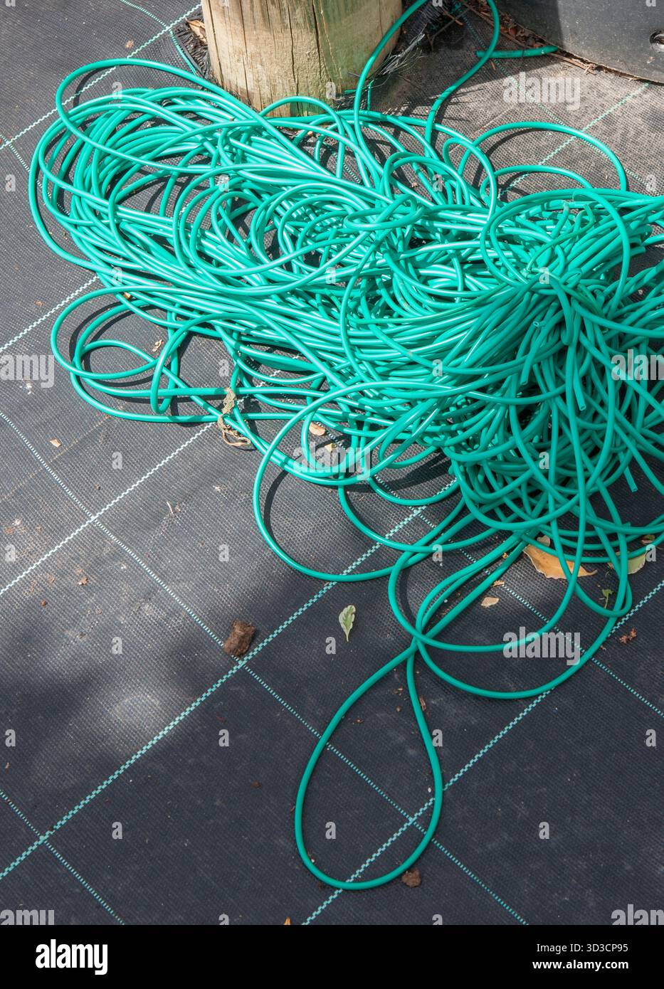 Flexibler Gartenbinderschlauch, der über der Unkrautmembran angezeigt wird. Versorgungskonzept für den Gartenbau Stockfoto