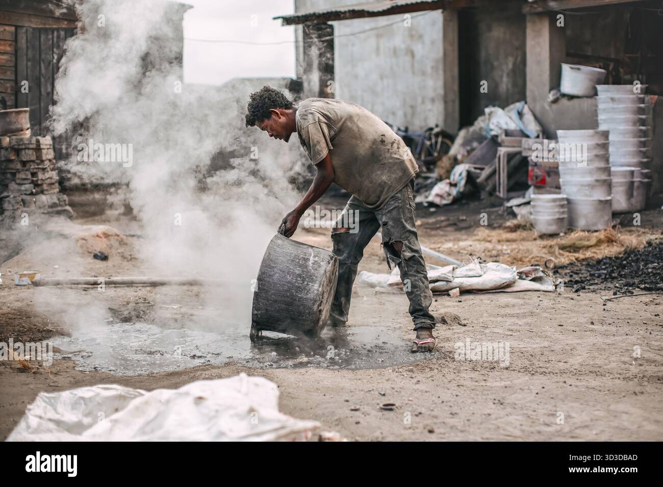 AAmbatolampy, Madagaskar - 25. April 2019: Aluminiumverarbeitungsfabrik, Dosen schmelzen in Töpfen über Feuer, Dampf oben, unbekannter Arbeiter Stockfoto