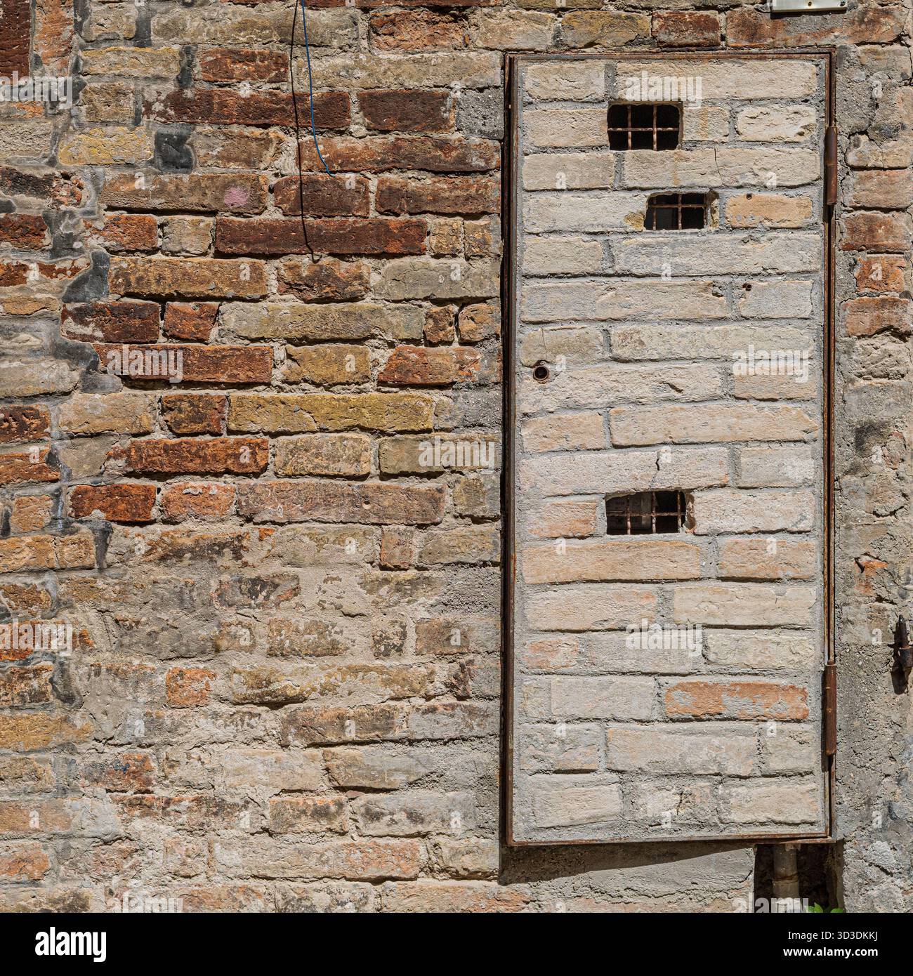 Tarnung: Die Tür eines kleinen Versorgungsraums muss sich in die umliegende Backsteinmauer einfügen. Urbino, Marken, Italien Stockfoto