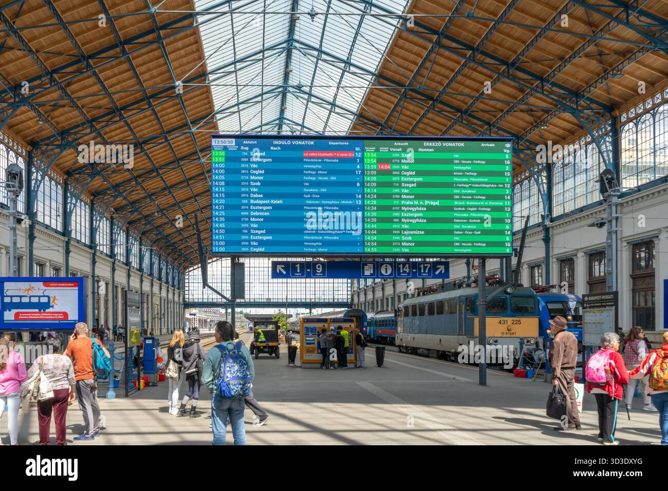 Geschäftige Bahnhofshalle Nyugati in Budapest mit großem digitalen Abfahrtstafel und Passagieren auf den Bahnsteigen. Stockfoto