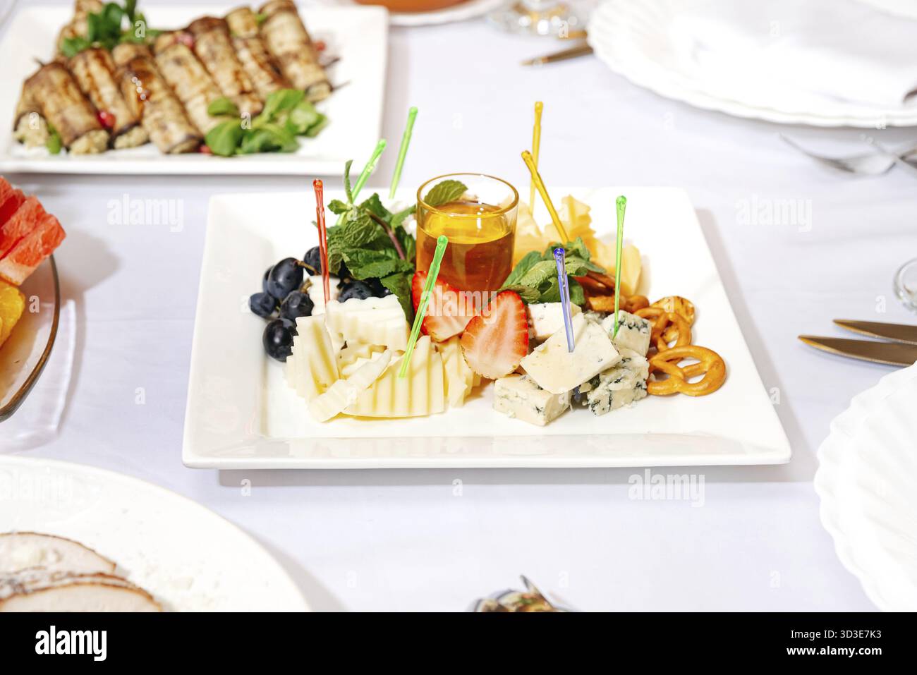 Essen, eleganter Vorspeiseteller mit verschiedenen Käsesorten, Trauben, Erdbeeren, Honig, Minzblättern, und knusprige Brezeln auf einer weißen Schale Stockfoto