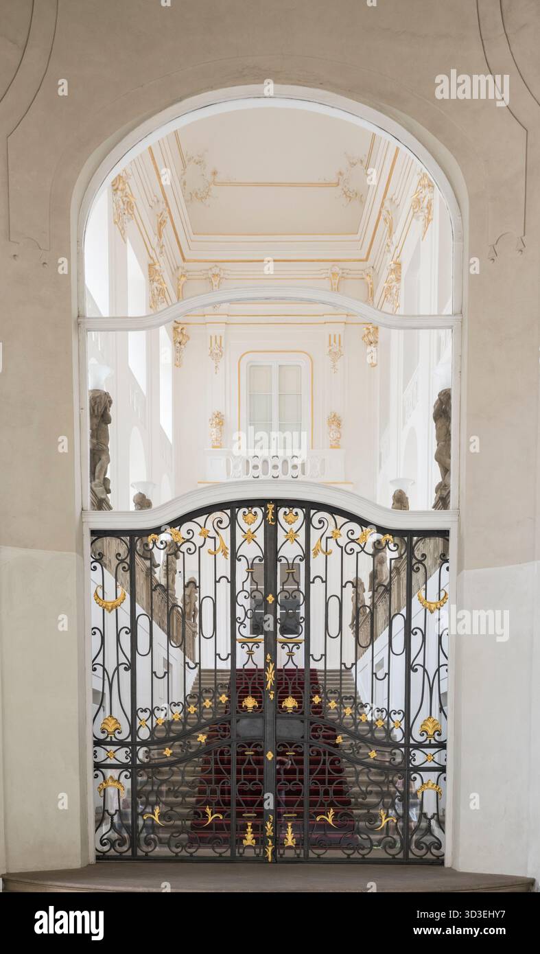Treppe mit rotem Teppichboden hinter einem kunstvoll verzierten schwarzen und goldenen Eisentor an der Prager Burg. Stockfoto