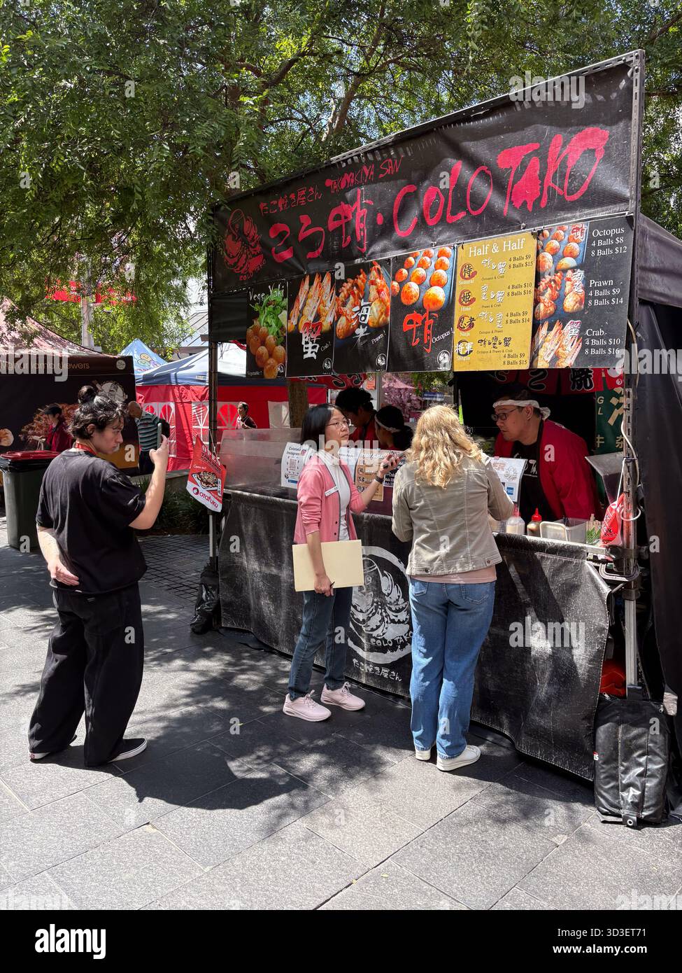 Street Food-Anbieter, der Takoyaki und andere Meeresfrüchte auf einem Markt im Freien in Chatswood, Australien, verkauft. Kunden interagieren mit dem Anbieter. Stockfoto