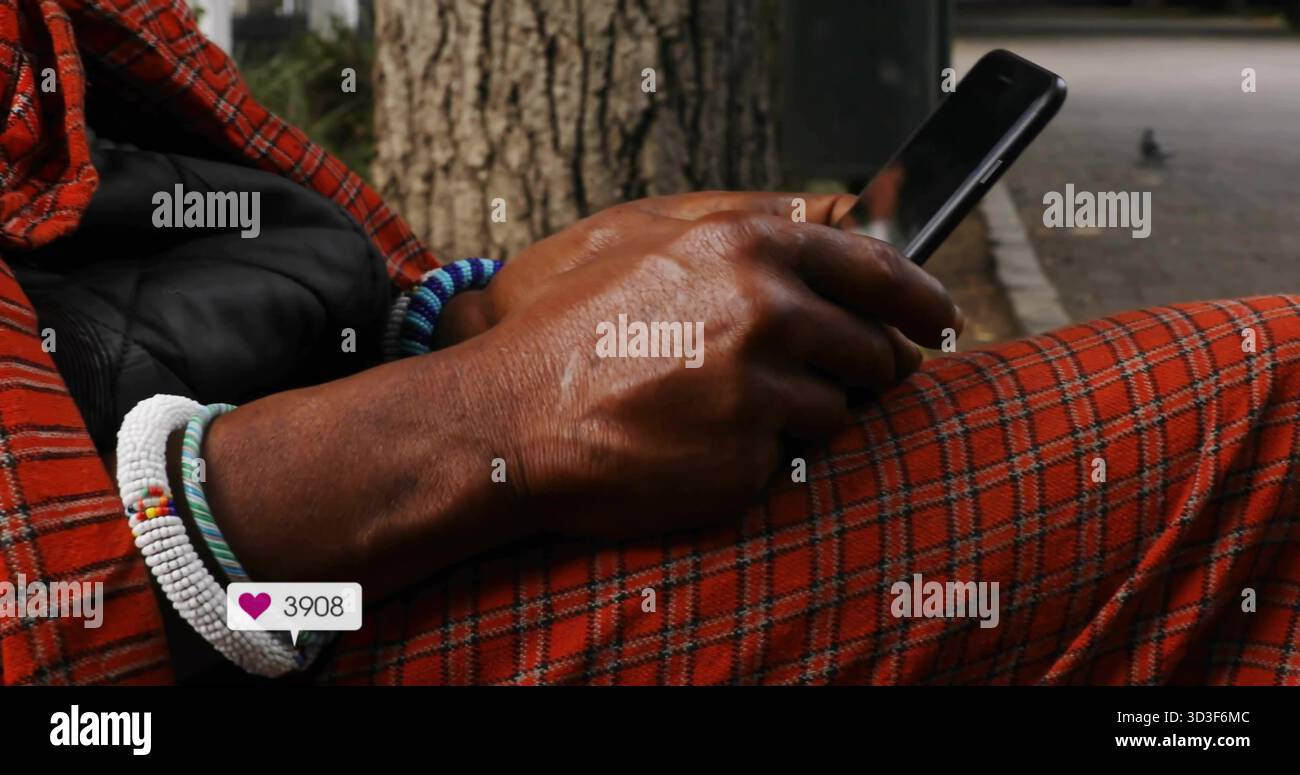 Scrollender Mann, der karierte Hosen neben dem Baumstamm trägt, mit einem Herzsymbol auf dem Telefon und den Armbändern Stockfoto