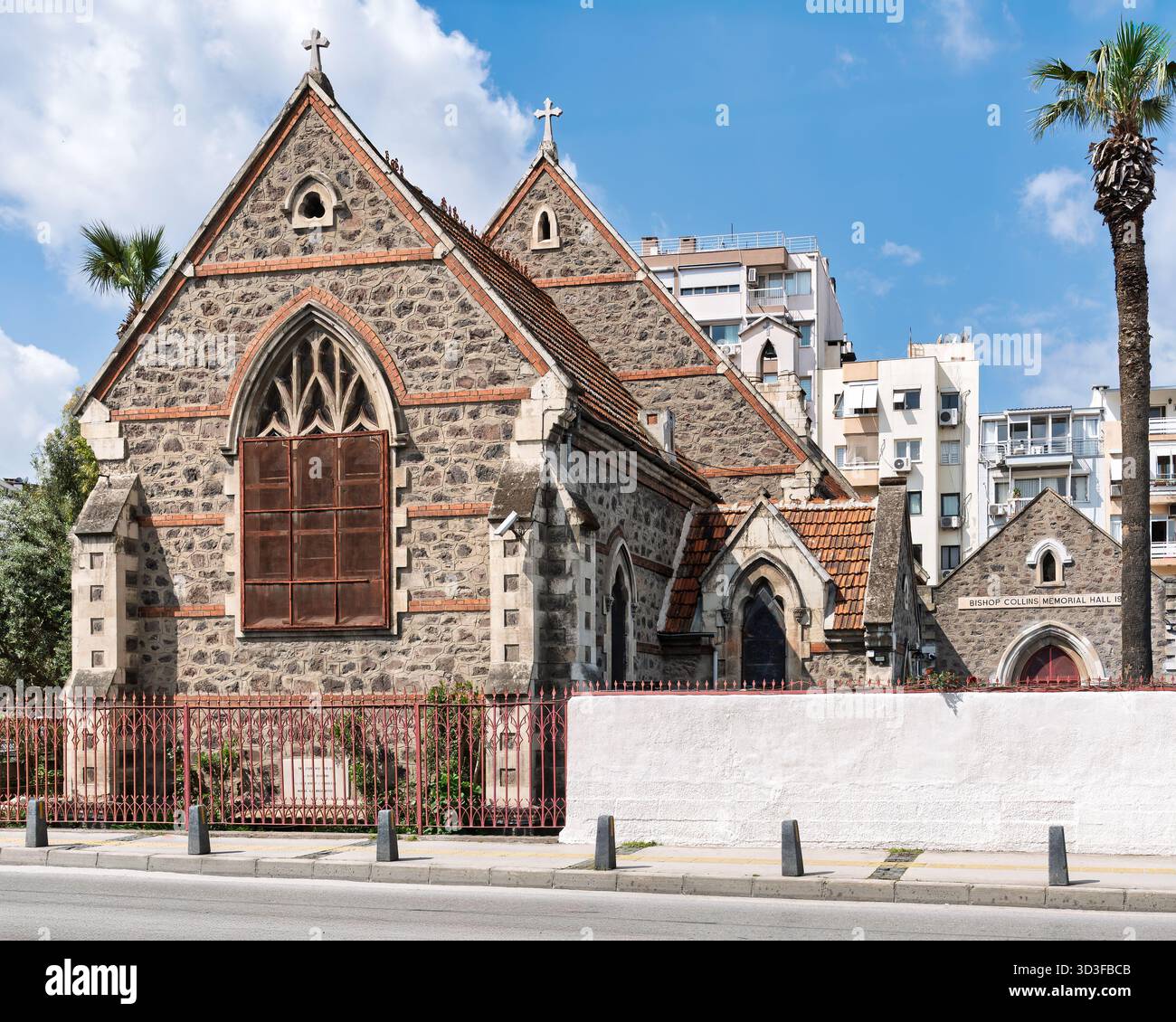 Bishop Collins Memorial Hall, St. John's Cathedral, Izmir, Türkei. Historische Steinkirche mit gotischen Fenstern, Dachkreuzen und Palmen an einem sonnigen Tag Stockfoto