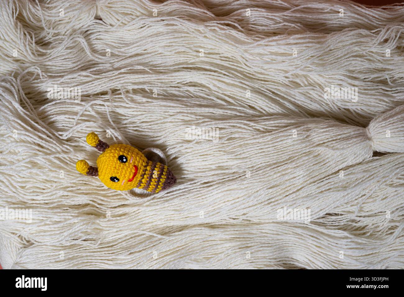 Handgefertigte Strickspielzeugbiene auf einem Bett aus weißem Garn Stockfoto